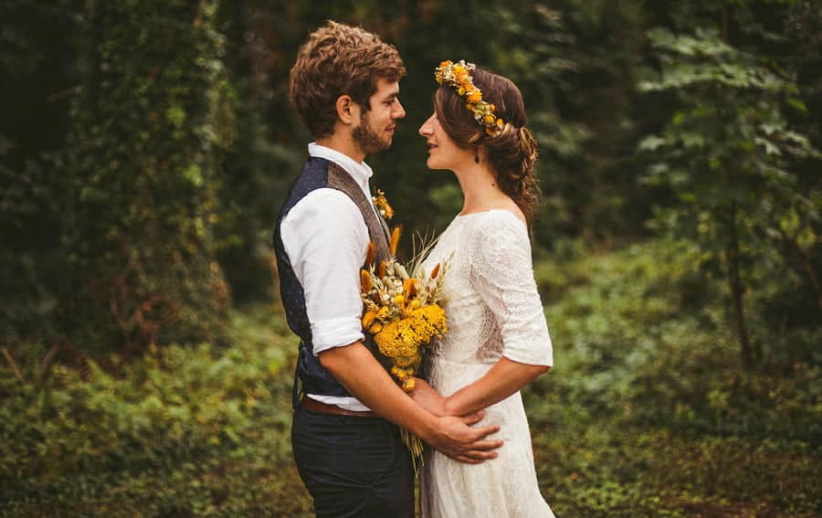 The bride and groom stand facing each other and smile with trees behind them