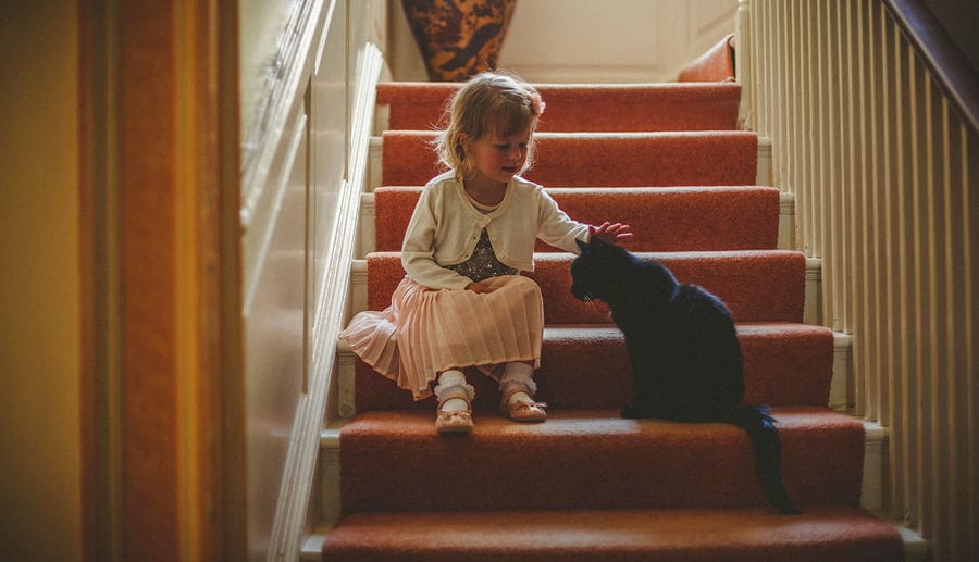A little girl sits on the stairs and strokes a black cat
