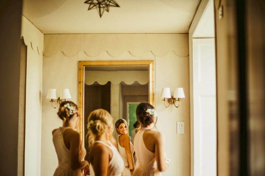 Bridesmaids looking into a large mirror hanging on a wall in the bathroom