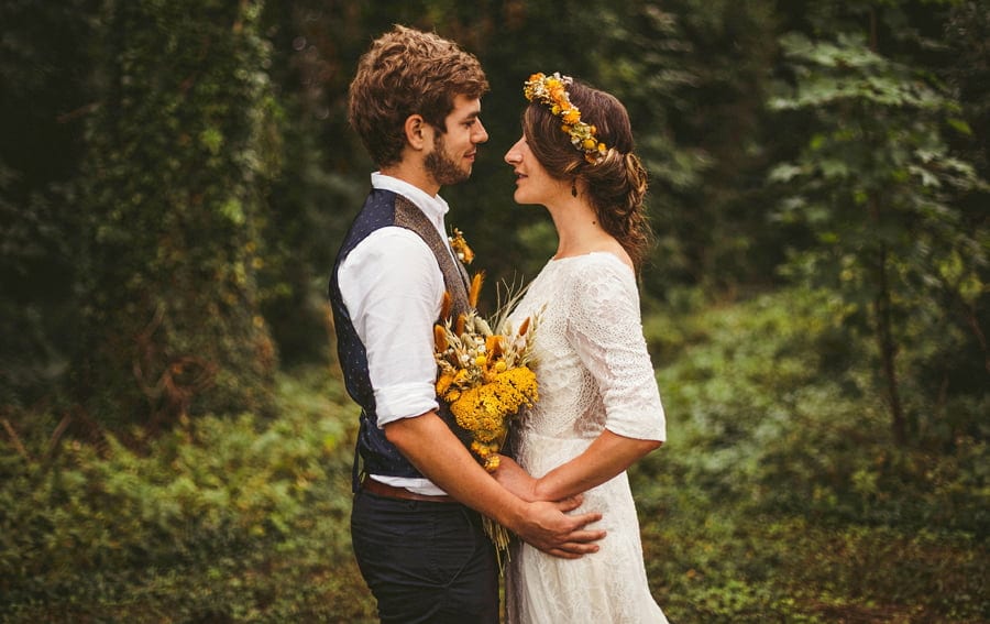 The bride and groom stand facing each other and smile with trees behind them