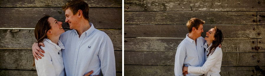A lady and a man embrace each other and laugh against a large wooden panel