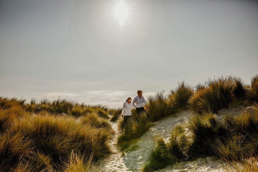 A man holds the lady's hand and walks along the sand dunes