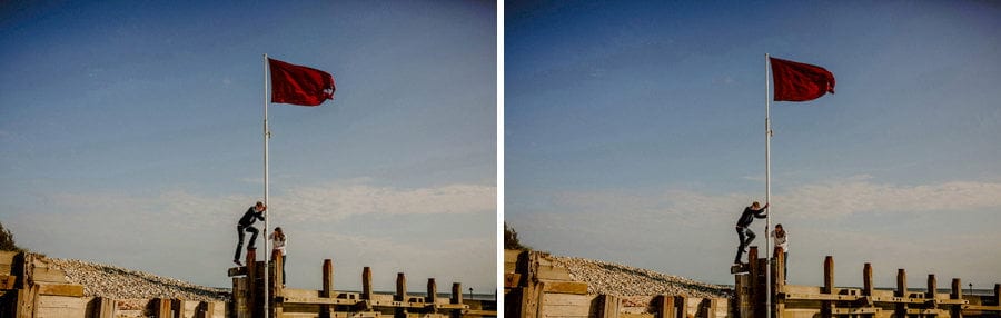 A lady and the man climb up a flagpole together on the beach at West Wittering