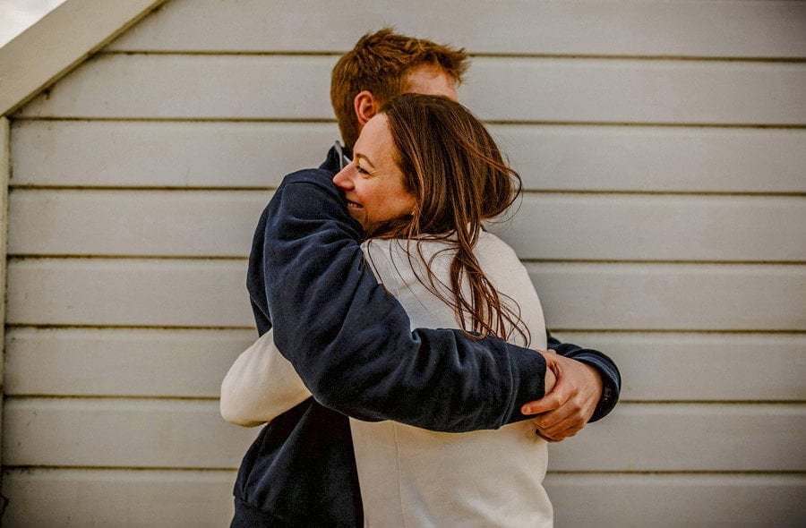 A man and lady embrace each other next to a beach hut on West Wittering beach