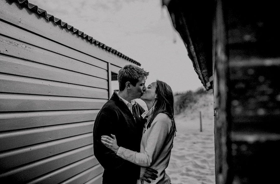 A man and lady kiss each other inbetween beach huts on West Wittering beach