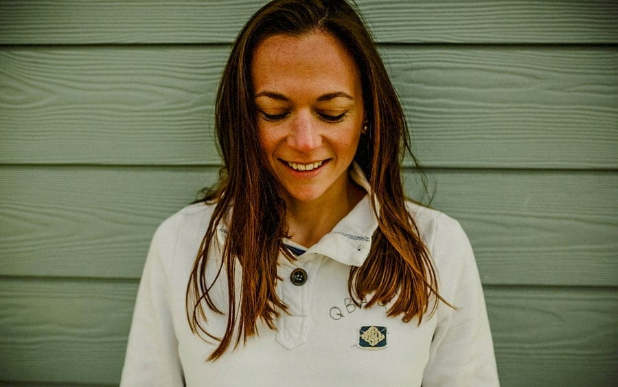 A lady looks down to the floor against a beach hut and poses for a photograph