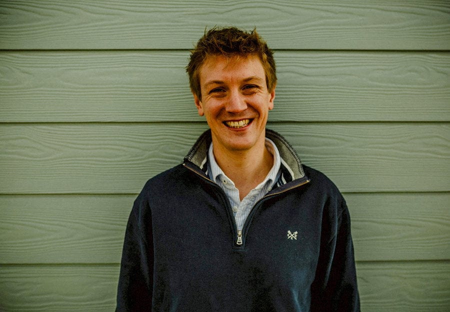 A man smiles and poses for a photograph stood next to a large green beach hut