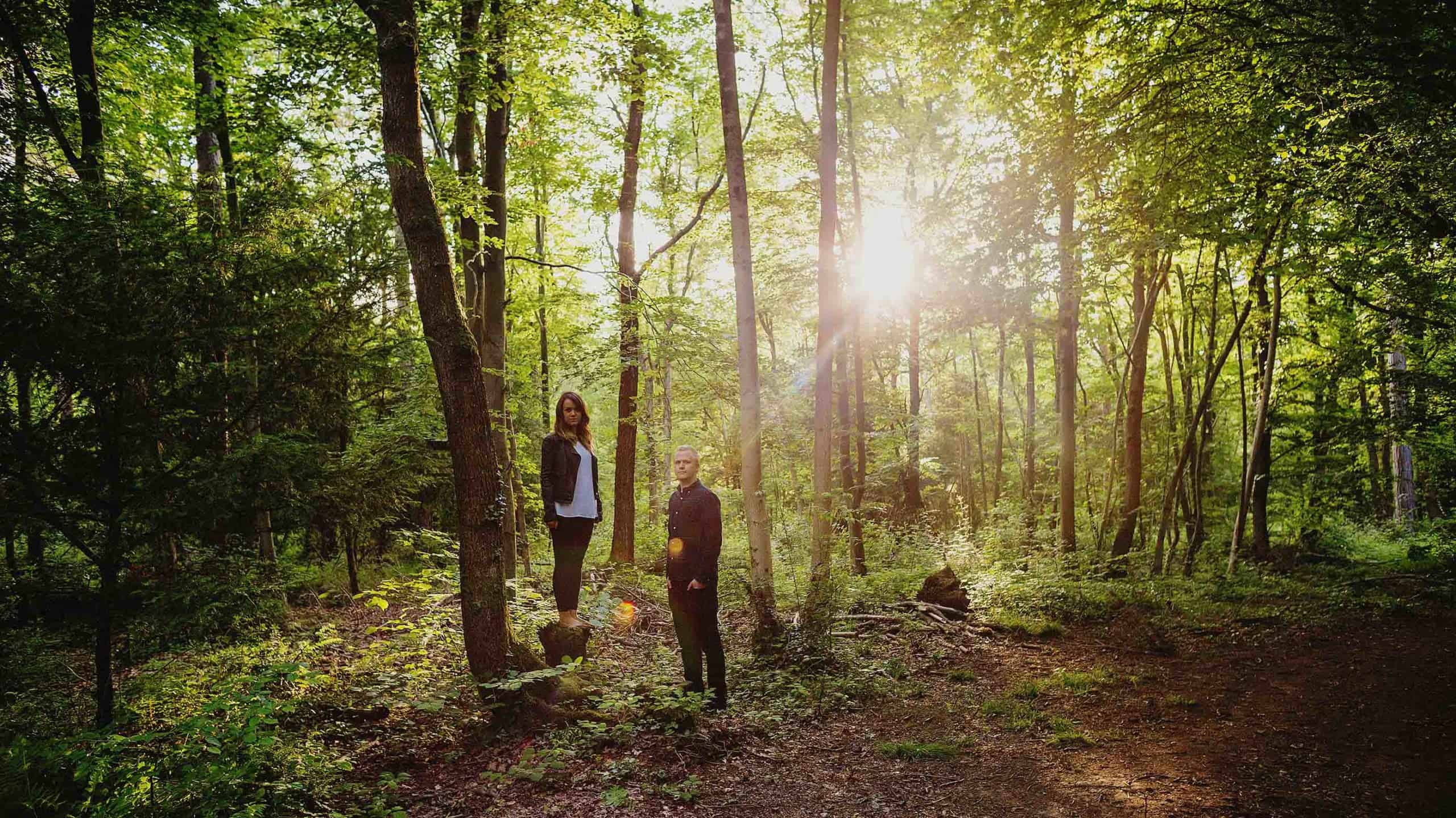 A man and lady stand next to each other and pose for a photograph in woods