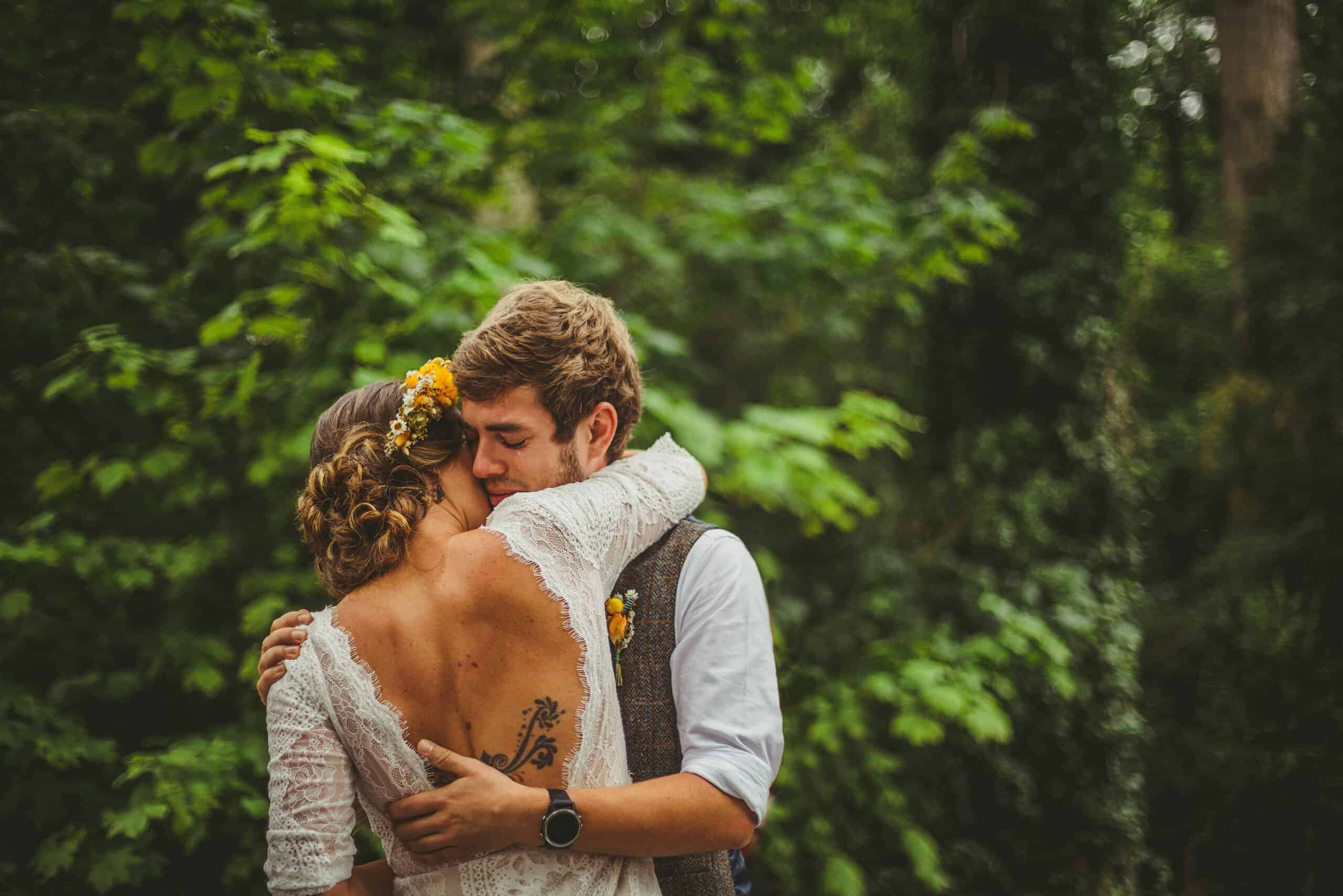 The bride places her arm around the groom as they greet each other in the woods for the outdoor wedding ceremony