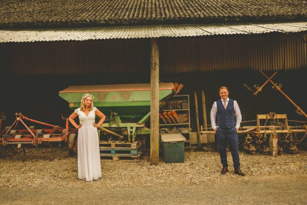 The bride and groom pose for a photograph in front of the barn at Over Barn in Gloucestershire