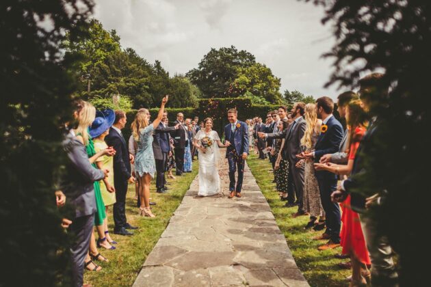 The bride and groom walk along the path in the gardens at Barley Wood house as wedding guests throw confetti in the air